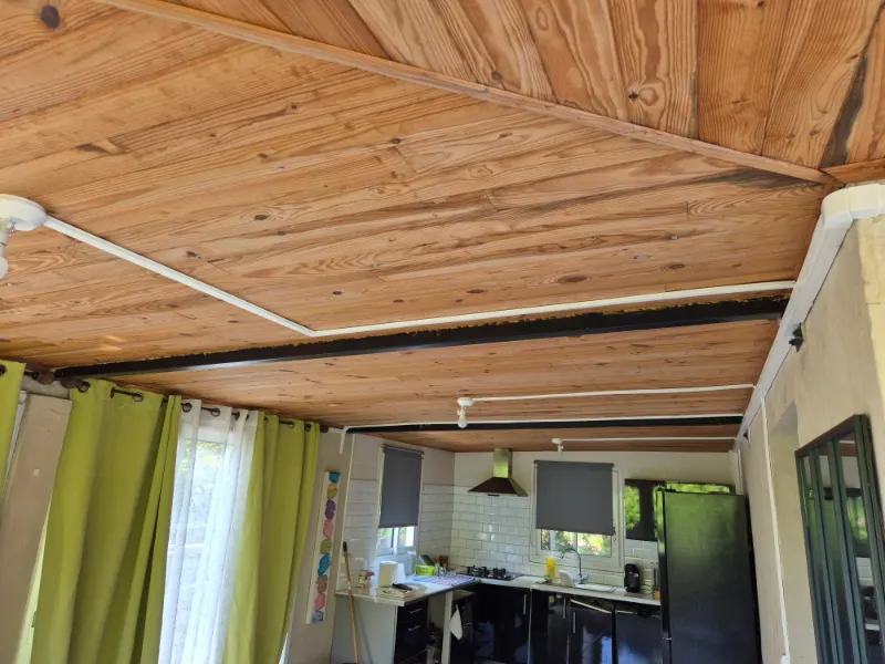 Un plafond en lambris de bois, des goulottes blanches qui mènent à plusieurs points de lumière jusqu'à la cuisine.
